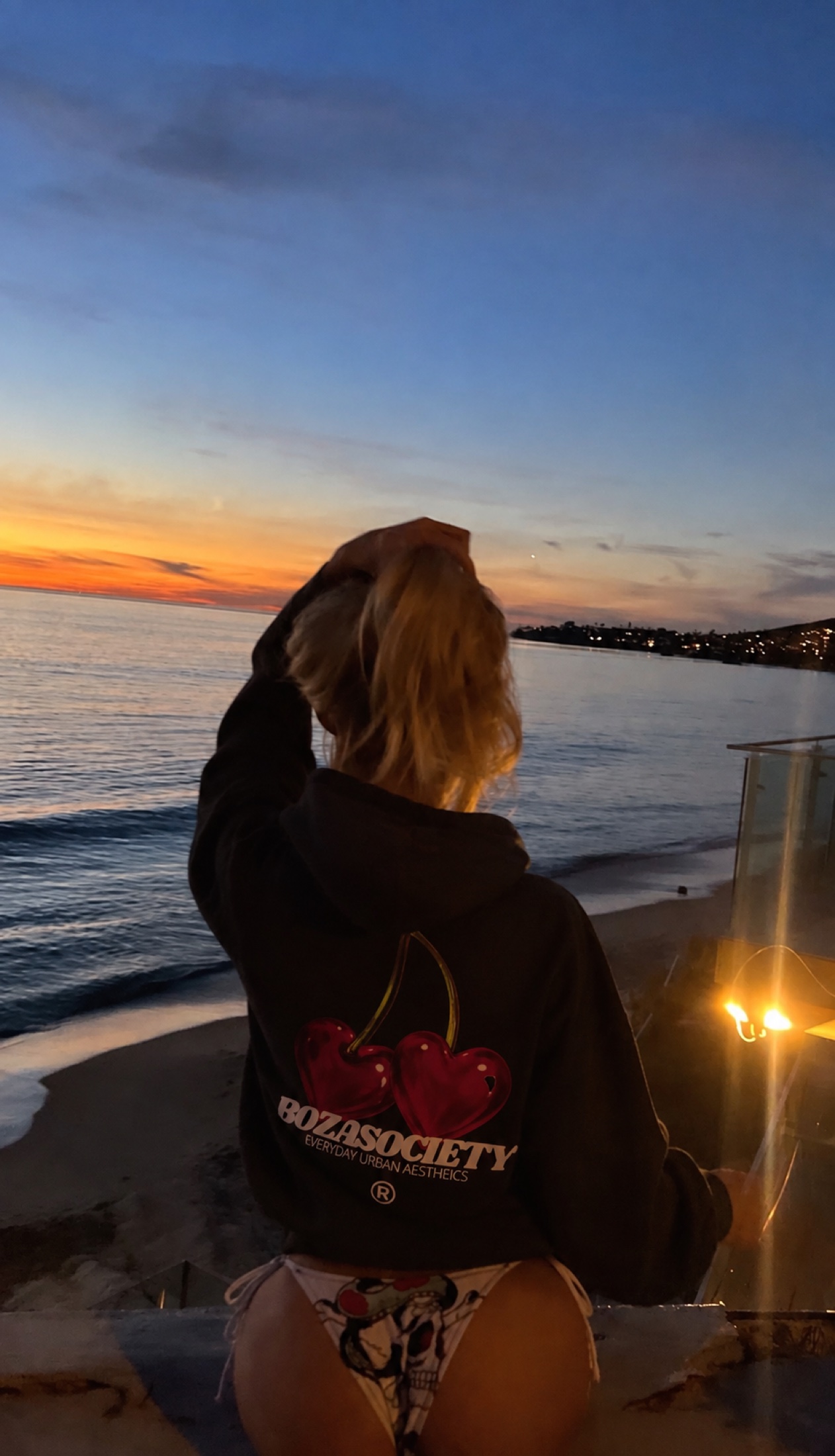 Mujer con hoodie BOZA negro frente al mar al atardecer